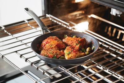 Oven-safe nonstick pan being used to finish off bone-in skin-on chicken thighs in the oven after being seared on the stove.
