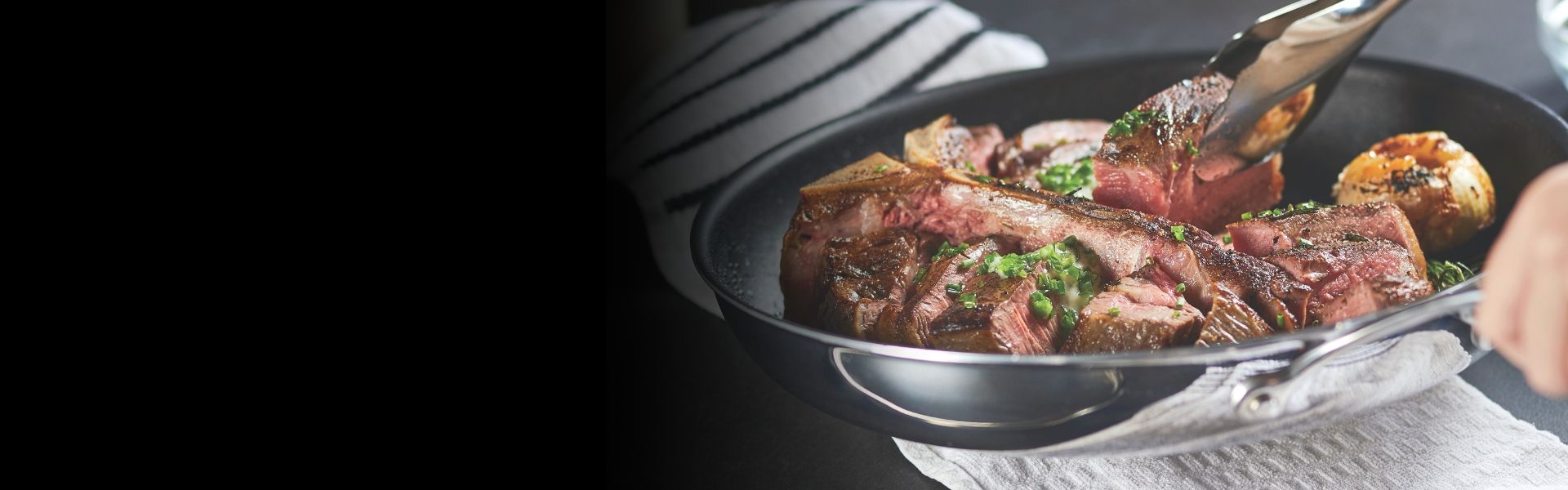 A skillet with sliced, cooked meat garnished with herbs, handled with tongs.