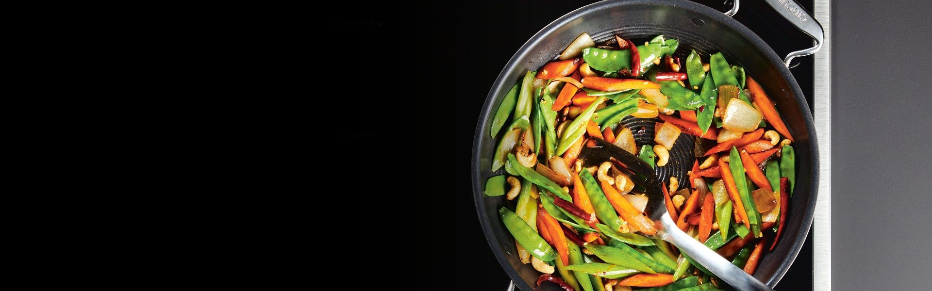 A skillet with stir-fried vegetables, including carrots, snap peas, and bell peppers, on a stove.