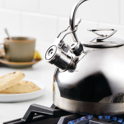 Stainless steel kettle on a gas stove with tea and biscotti in the background.