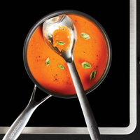 Tomato soup with basil leaves in a pot, with a ladle on a black background.
