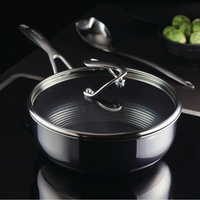 Stainless steel pan with glass lid on stovetop, spoon, and Brussels sprouts nearby.
