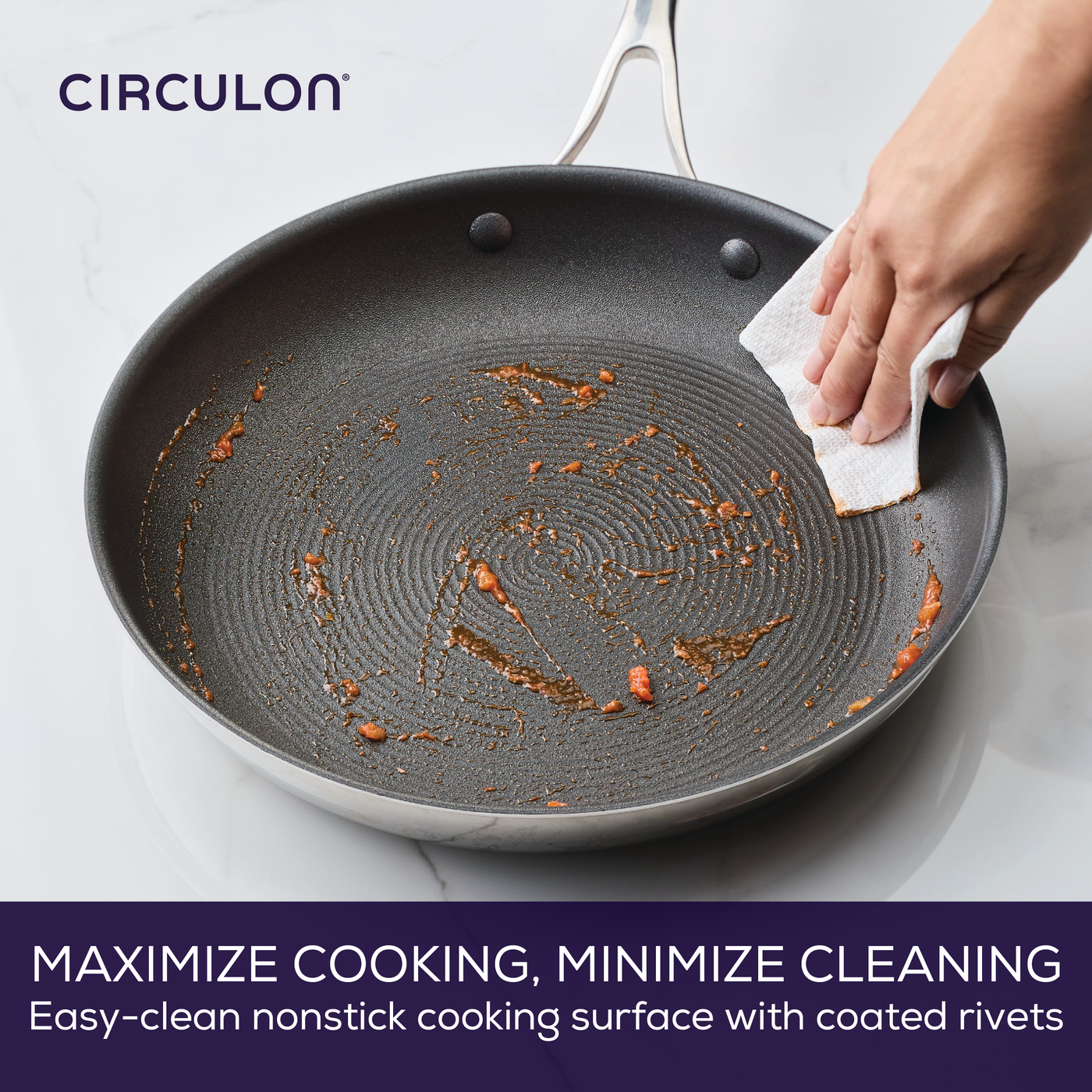 Hand wiping a nonstick pan with a cloth over a marble surface.