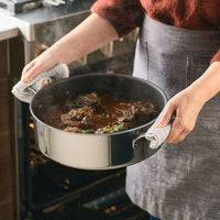 Person holds C1 Series ScratchDefense Nonstick 7-Quart Braiser with Lid by oven.
