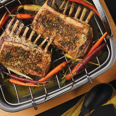 Two seasoned racks of lamb with carrots in a roasting pan.