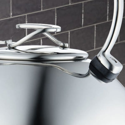 Silver kettle with a black handle against a dark tiled background.