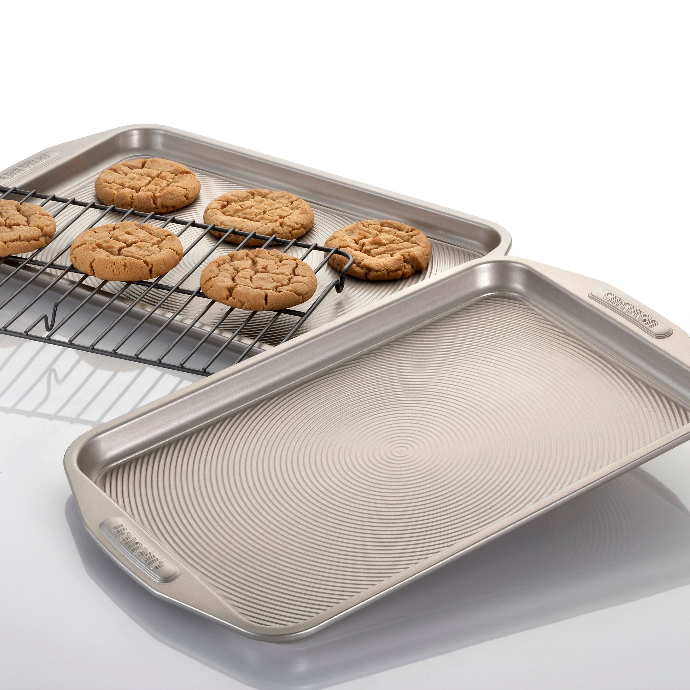 Cookies rest on a cooling rack beside an empty textured sheet pan from the Nonstick Bakeware Set, its advanced nonstick system ensuring effortless cleanup.