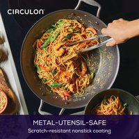 Someone cooking pasta with shrimp and vegetables in a nonstick pan.