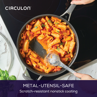 Pasta cooking in a nonstick pan on a stove, stirred with a metal utensil.