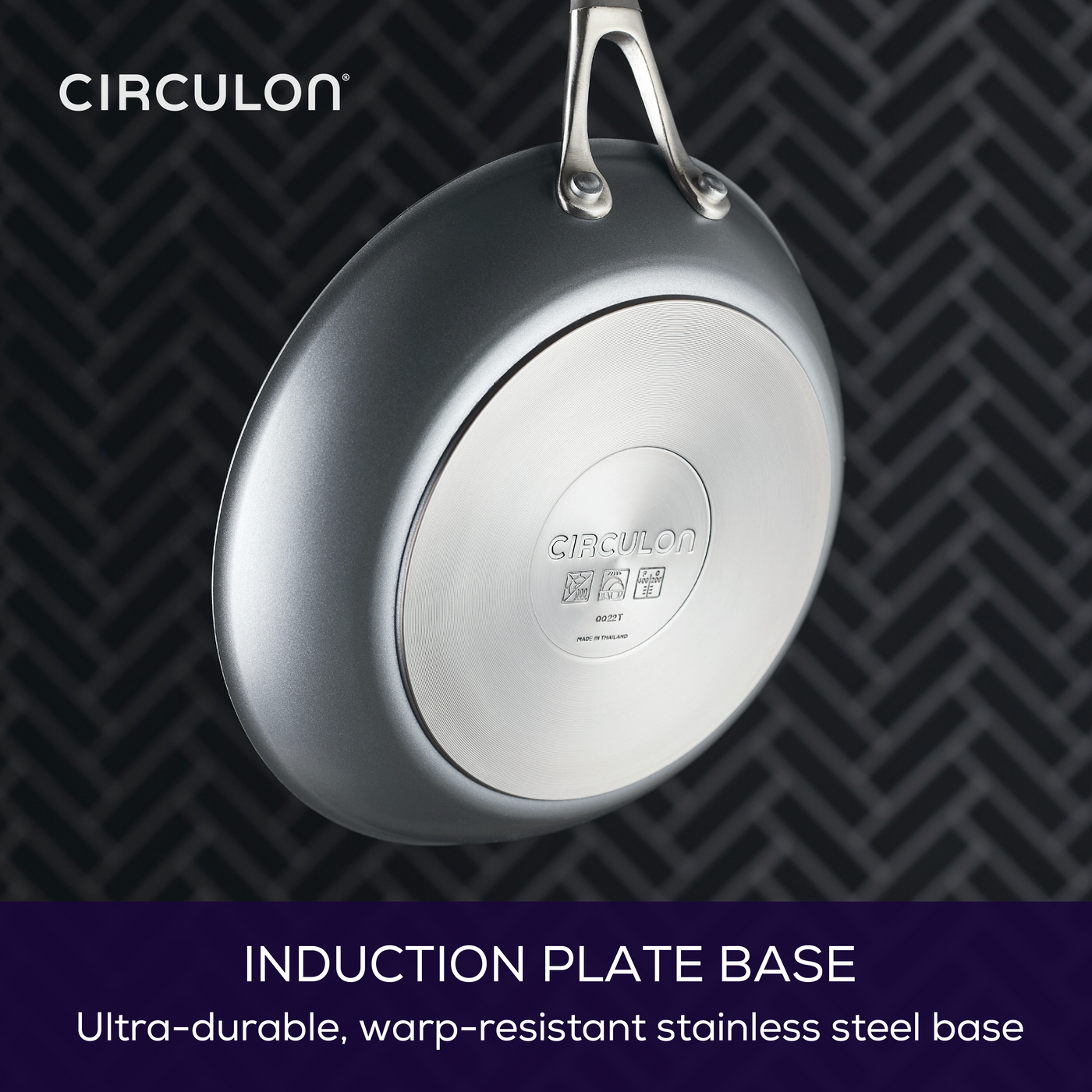 A frying pan with an induction plate base hangs against a patterned background.