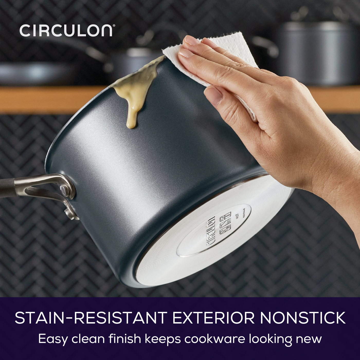Hand wiping a blue nonstick saucepan with a white cloth.