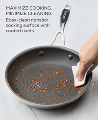 Hand cleaning a nonstick frying pan with a sponge on a marble surface.
