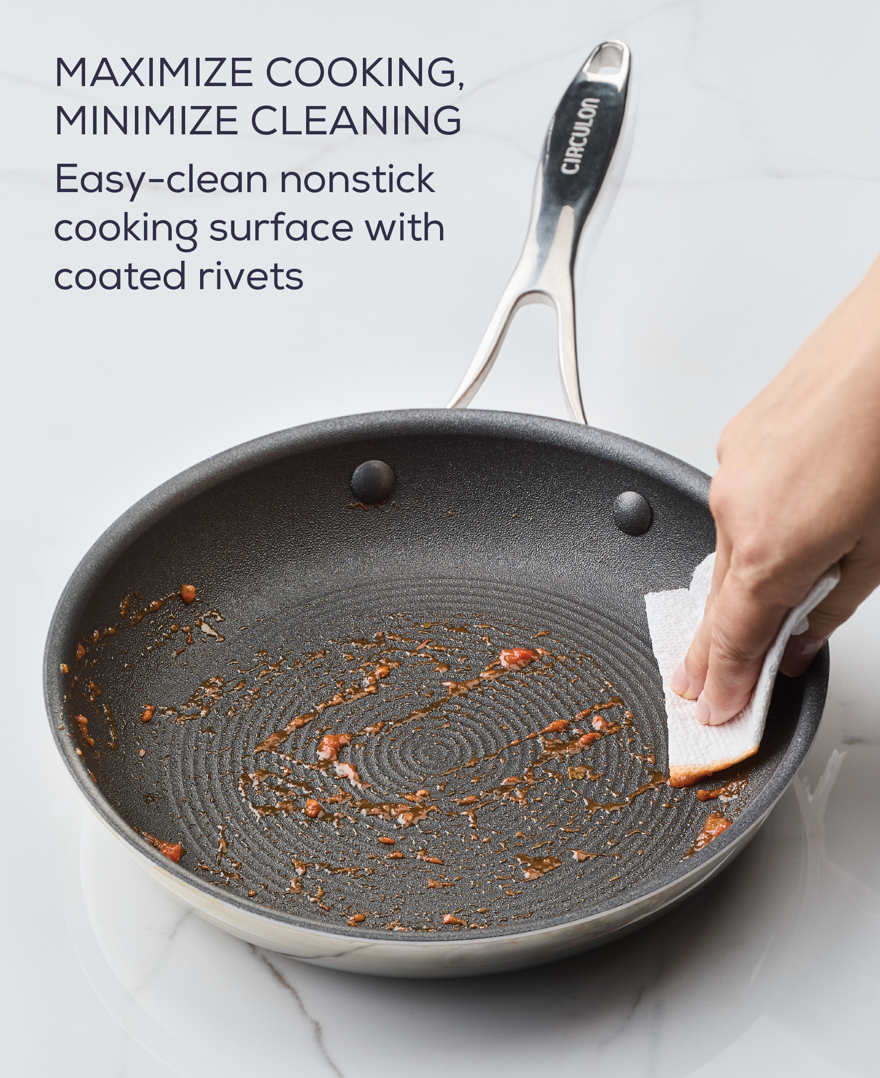 Hand cleaning a nonstick frying pan with a sponge on a marble surface.