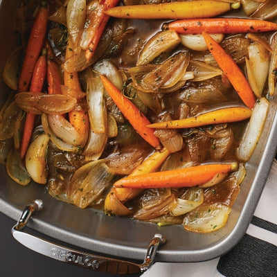Roasted carrots and onions in a baking dish with herbs.