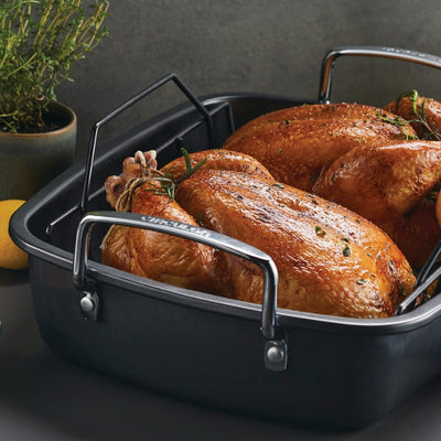 Roasted chicken in a black roasting pan with herbs.