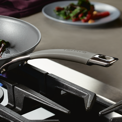Close-up of a saucepan handle on a stovetop with food in the background.