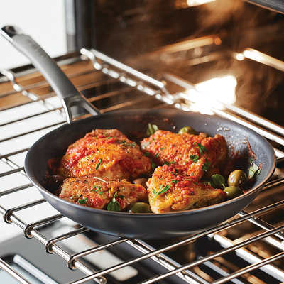 Chicken thighs with olives in a skillet inside an oven.