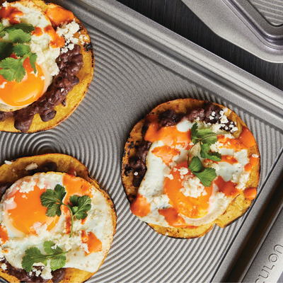 Three huevos rancheros on a griddle with eggs, salsa, beans, and cilantro.