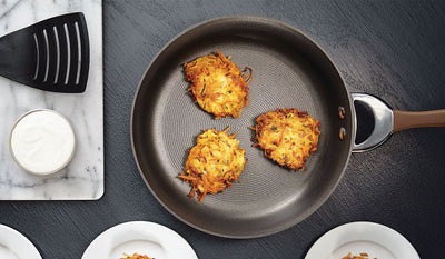 Three potato pancakes in a pan beside sour cream on a marble tray.