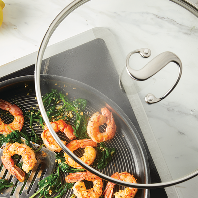 Shrimp and spinach cooking in a pan under a glass lid on the stove.