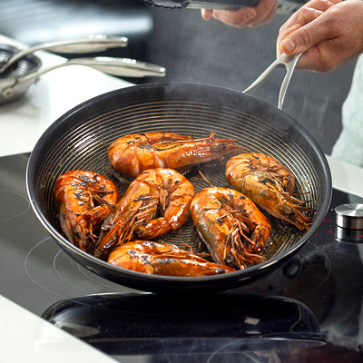 Person cooking large prawns in a pan on a stovetop.