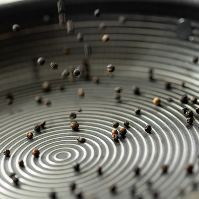 Black peppercorns falling into a circular grooved dish.