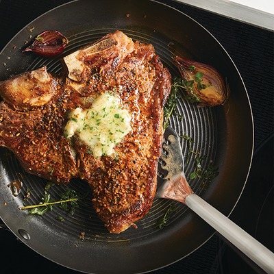 Steak with herbed butter in a skillet, garnished with onions and herbs.