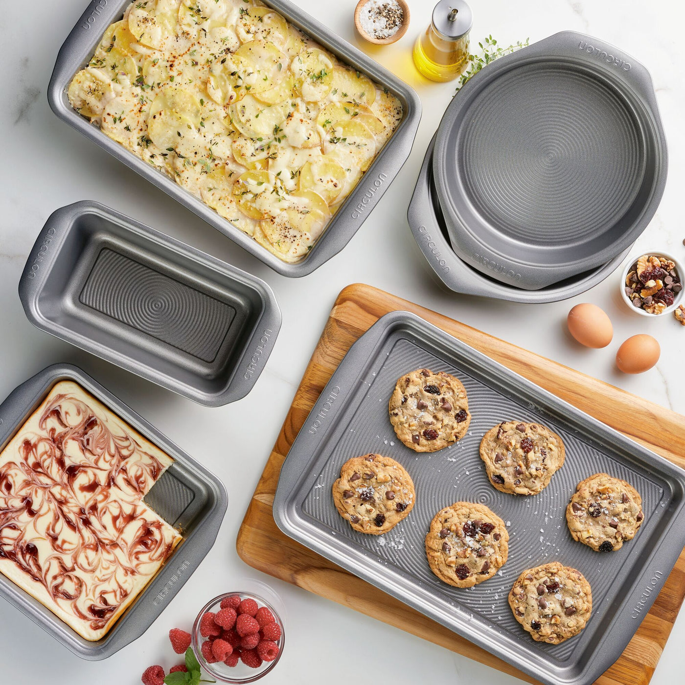 Various baked goods in metal baking pans on a wooden and marble surface.