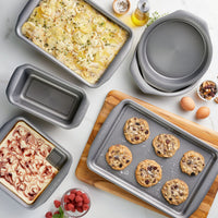 Various baked goods in metal baking pans on a wooden and marble surface.