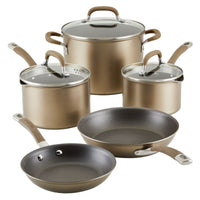 Set of five gold-colored pots and pans with glass lids and handles.