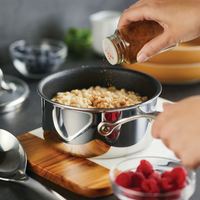 Cinnamon being sprinkled into a pot of oatmeal on a cutting board.