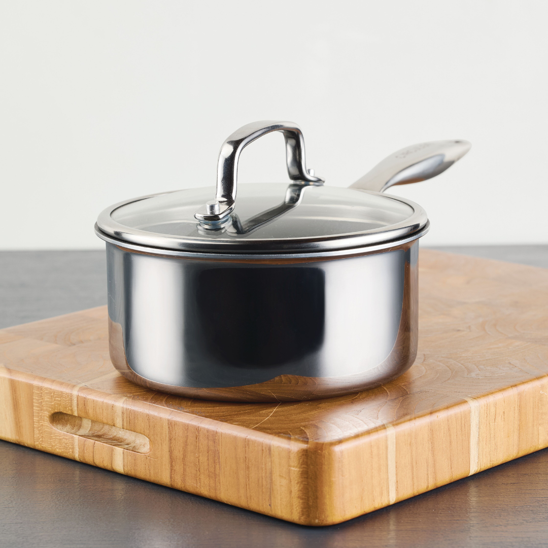 A stainless steel saucepan with a lid on a wooden cutting board.