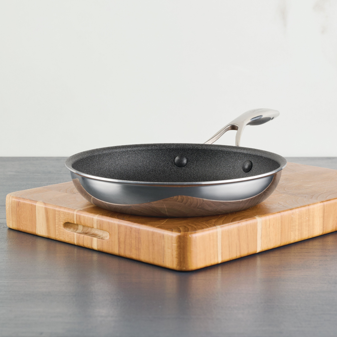 A frying pan on a wooden cutting board on a dark countertop.