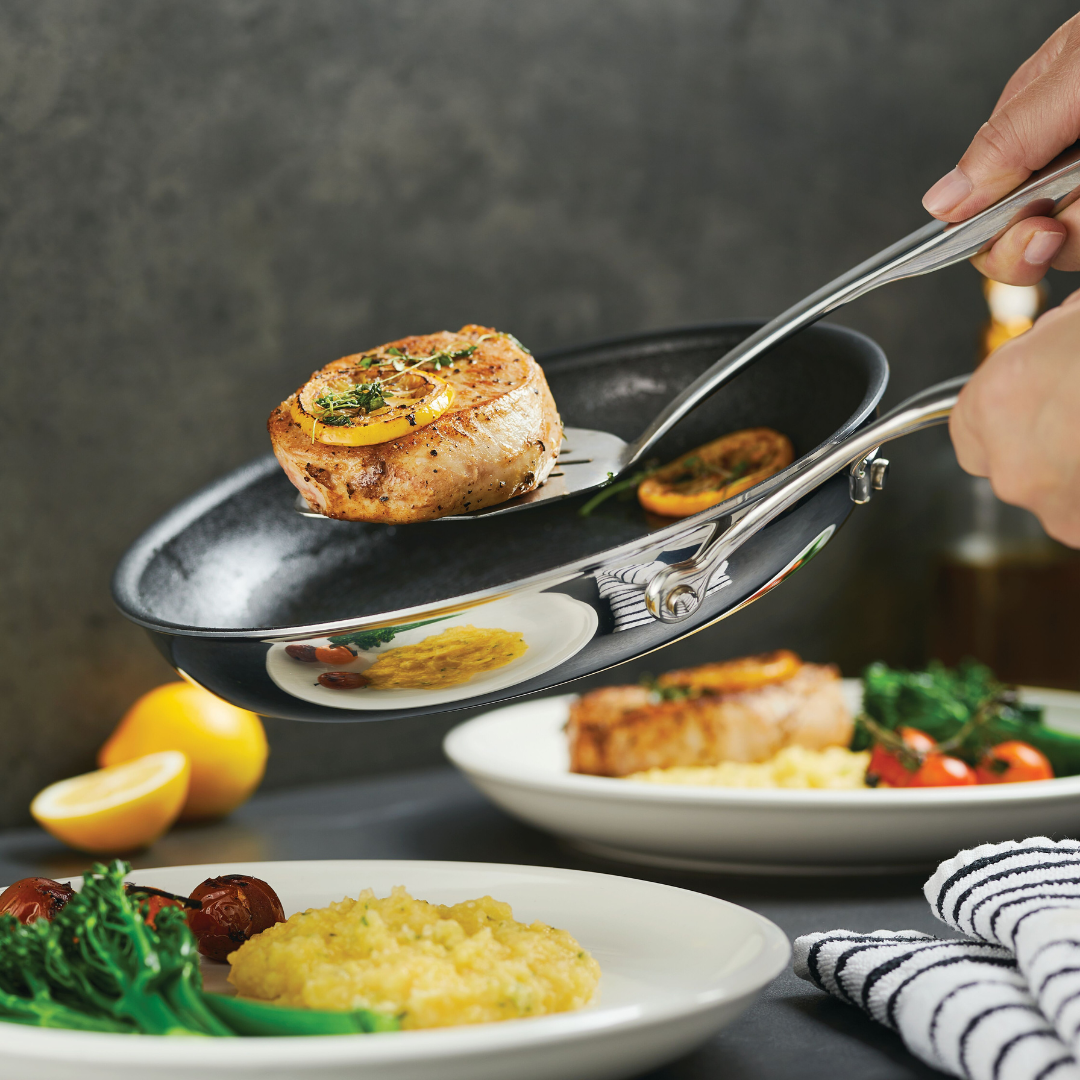 Hands transfer cooked food from a pan to a plate.