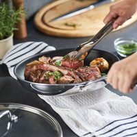 Person using tongs to cook and arrange meat in a pan on a stovetop.