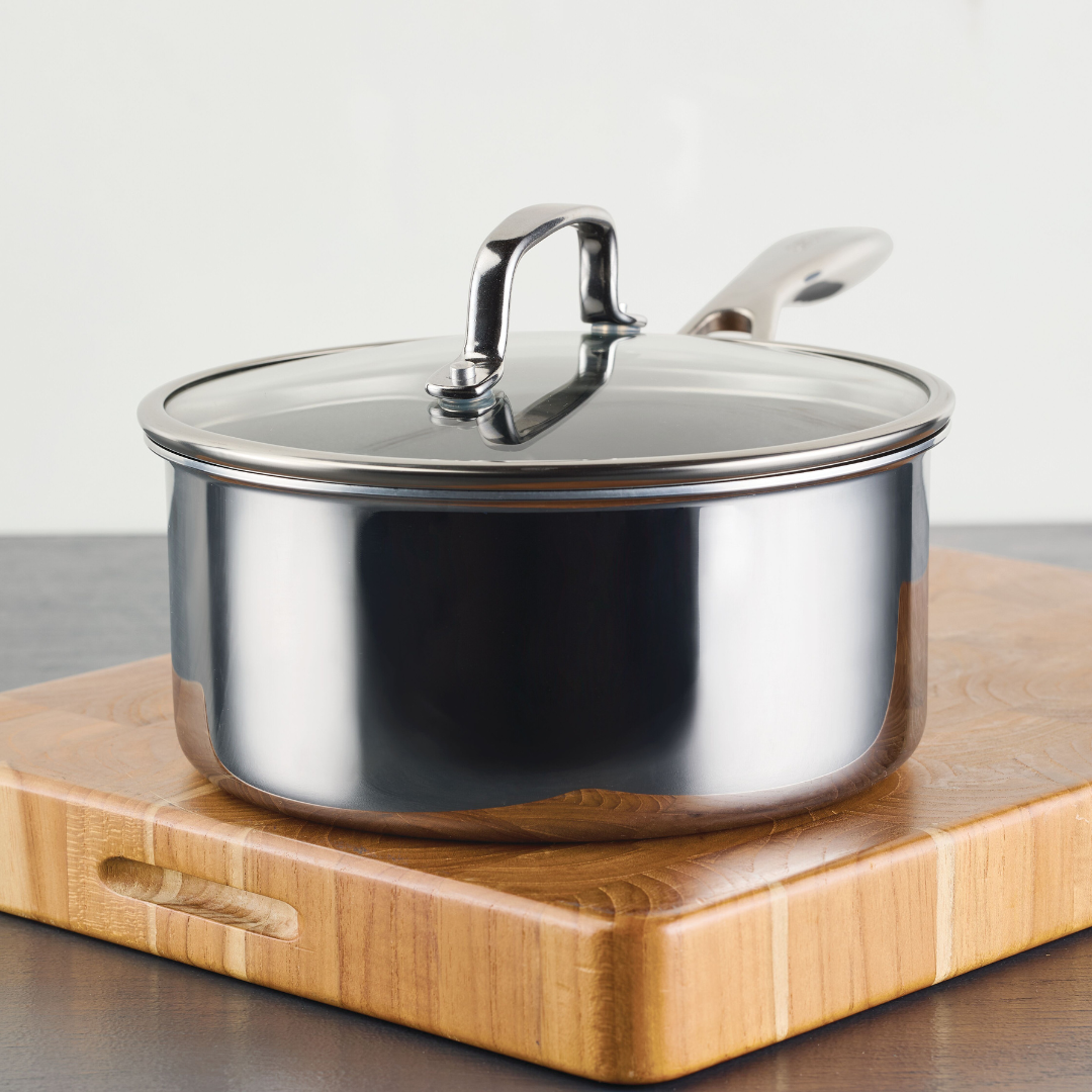 Stainless steel saucepan with lid on a wooden cutting board.