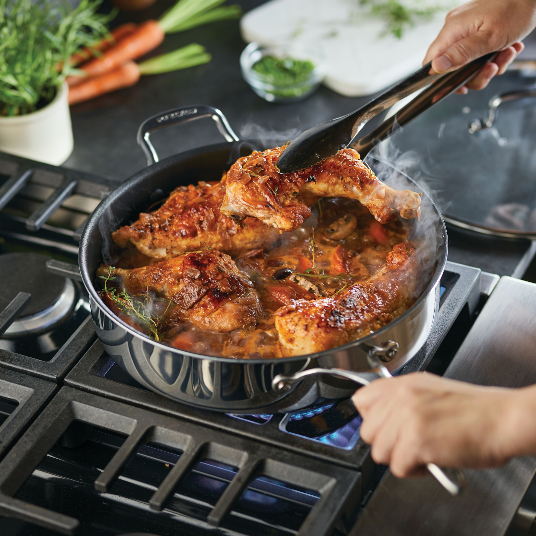 Person cooking chicken in a pan on a stove with vegetables.