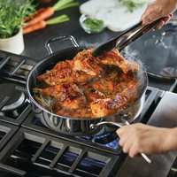 Person cooking chicken in a pan on a stove with vegetables.