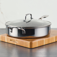 Stainless steel frying pan with lid on a wooden cutting board.