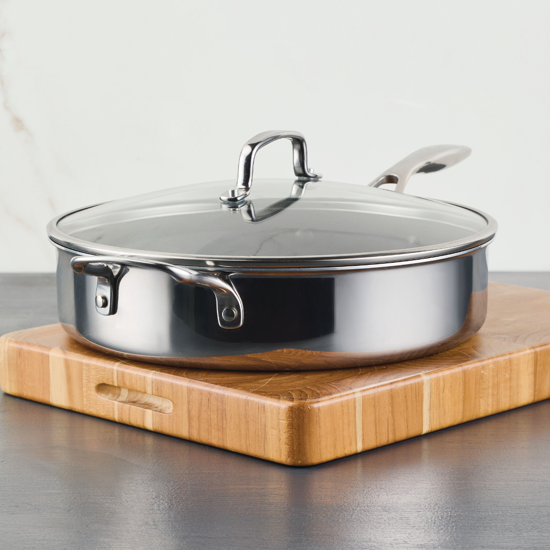 Stainless steel frying pan with lid on a wooden cutting board.