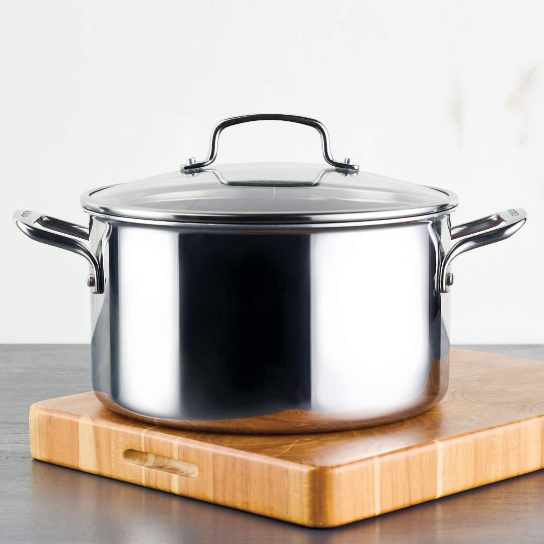 Stainless steel pot with a lid on a wooden cutting board.