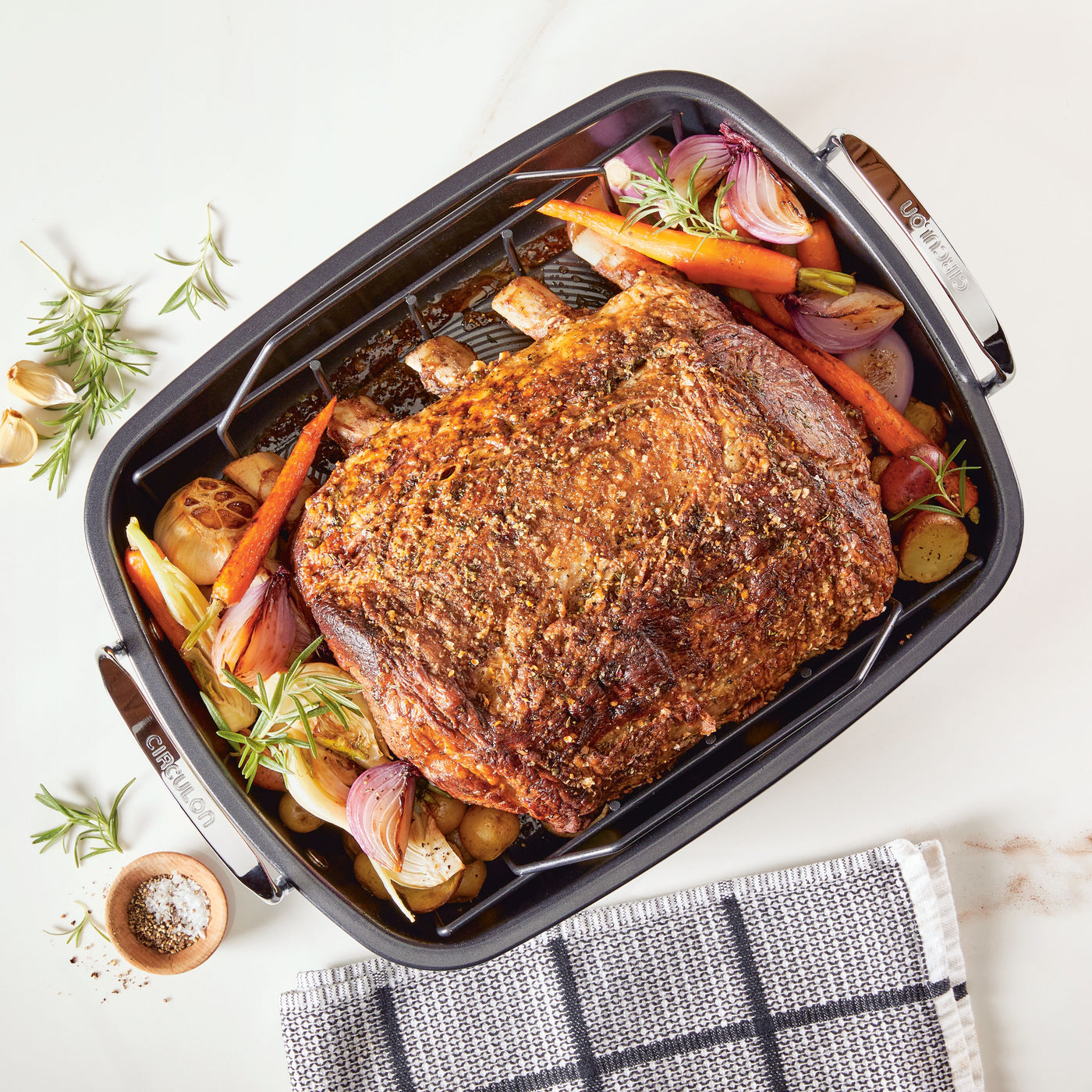 Juicy roasted meat with vegetables rests in the Roasting Pan: Nonstick Roaster Pan with Easy Serve Rack, elegantly presented on a white surface.