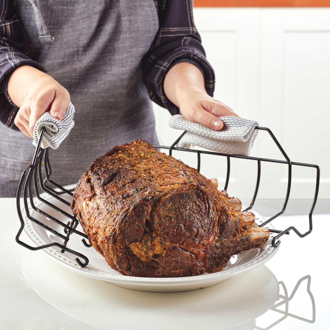 Using the Nonstick Roaster Pan with Easy Serve Rack, a person expertly places a cooked rib roast on a plate.