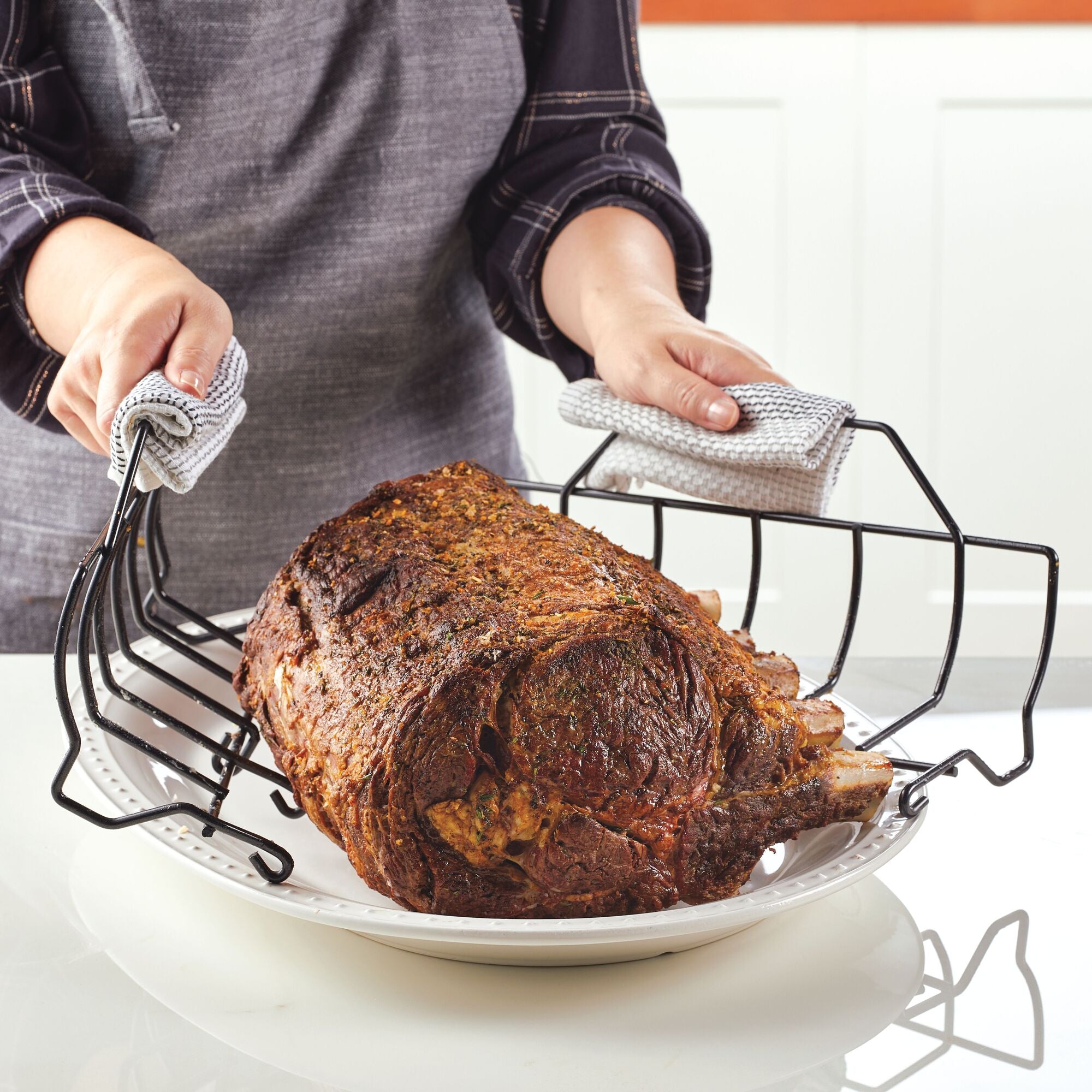 Using the Nonstick Roaster Pan with Easy Serve Rack, a person expertly places a cooked rib roast on a plate.