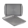 Displayed on a white background, the 2-Piece Nonstick Cookie Sheet Set features two metal baking trays, with one slightly tilted. These oven-safe pans guarantee effortless baking and easy cleanup.