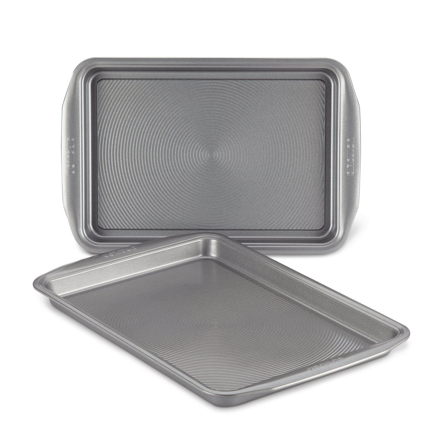 Displayed on a white background, the 2-Piece Nonstick Cookie Sheet Set features two metal baking trays, with one slightly tilted. These oven-safe pans guarantee effortless baking and easy cleanup.