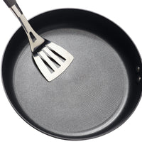 A Hard-Anodized Frying Pan Set with a nonstick system includes a metal spatula resting on its surface.